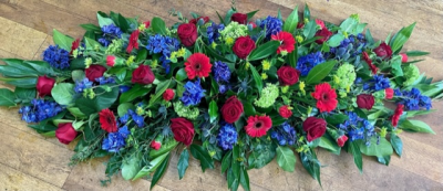 Regal Rose - A beautiful deep red and blue spray, consisting of velvety roses, delphinium, gerberas and thistle, plus much more. Hints of lime green lift the colours and finish this truly stunning tribute.