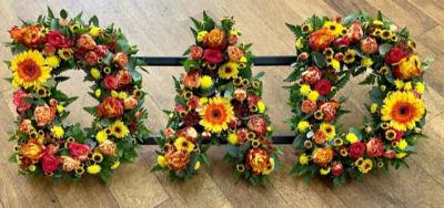 Dad 10 - Loose lettering, meaning that the letters are filled with greenery and mixed dainty flowers. This "Dad" tribute consists of beautiful warm orange, yellow and red seasonal flowers. Any wording can be created in this style, and colours can be altered to suit your preferences- please call us to discuss. £45.00 per letter.