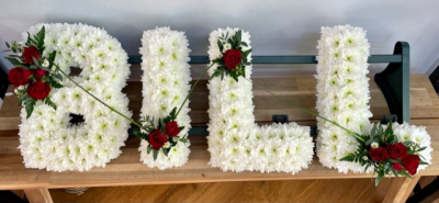 Four-letter name tribute (Bill) - Example lettering "Bill" massed in white chrysanthemums with red rose sprays on each letter with decorative grass loops. 
Any wording can be created in this style, and colours can be altered to suit your preferences- please call us to discuss your requirements or note your four-letter name in the "any special requests" box to order online. 
£45.00 per letter.