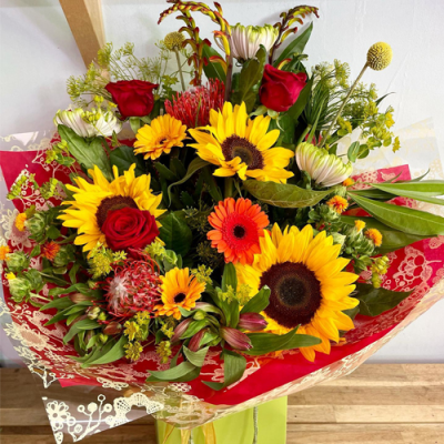 Hello Sunshine - A sunny handtied bouquet in water presented in a gift bag/box. Created using yellow, red, orange and white flowers with complimentary foliage.